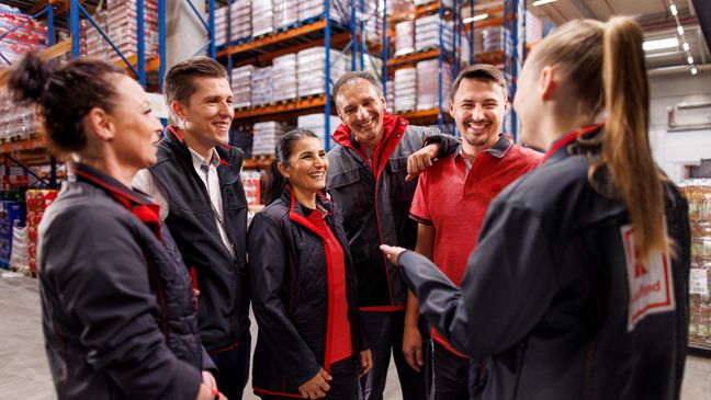 Sechs Logistikmitarbeiter von Kaufland im Gespräch. Im Hintergrund volle Lagerregale.