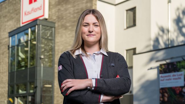 Hausleiterin steht vor einer Kaufland-Filiale mit verschränkten Armen und lächelt.