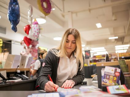 Hausleiterin unterschreibt ein Dokument an der Information einer Kaufland-Filiale.