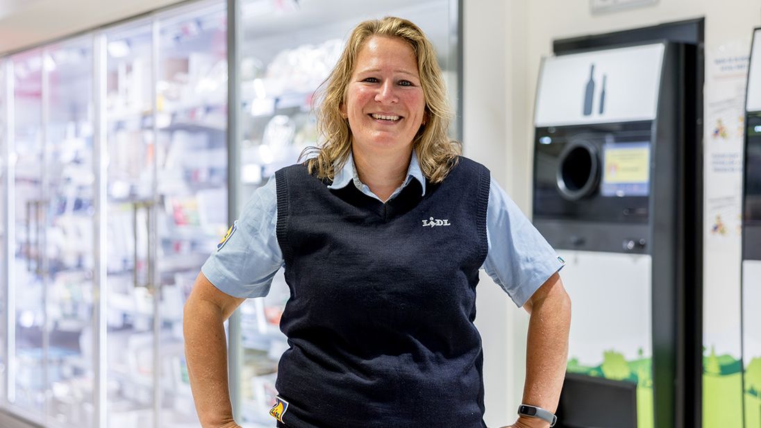 Glimlachende Lidl supermarktmanager voor een flessenautomaat
