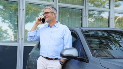 Knut Harenkamp Kaufland Manager telefoniert entspannt am Firmenwagen, im Hintergrund moderne Bürogebäude.