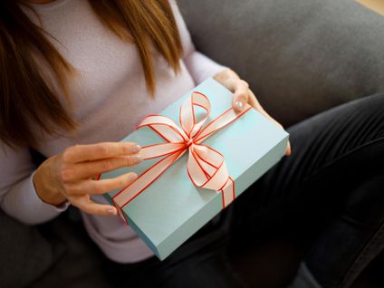 Frau sitzt auf einem Sofa und hält ein blau verpacktes Geschenk in der Hand.