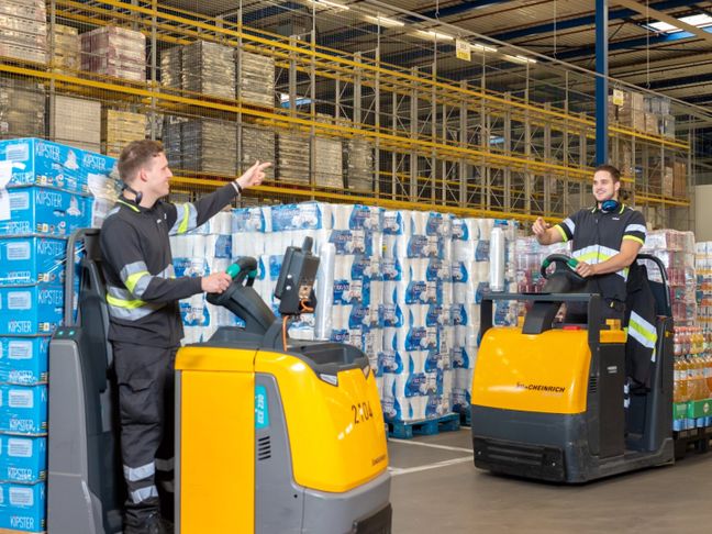 Twee hulpkrachten op een elektrische pompwagen in het distributiecentrum