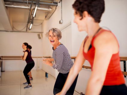 Zwei Frauen nehmen an einem Fitnesskurs teil und lachen dabei. Im Hintergrund sieht man weitere Teilnehmer.