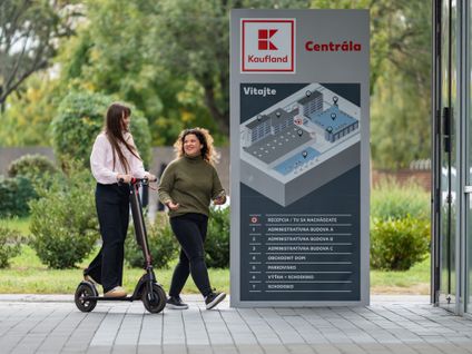 Študentka a brigádnička na kolobežke pred vchodom do centrály