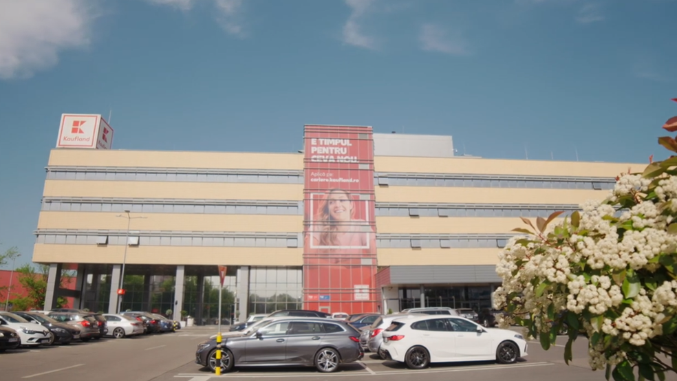 Clădire de birouri Kaufland cu o parcare în față și un banner de recrutare pe care scrie „E timpul pentru ceva nou”.