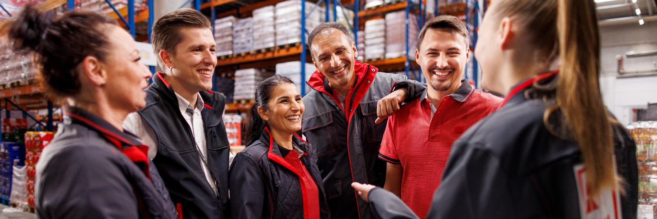 Sechs Logistikmitarbeiter von Kaufland im Gespräch. Im Hintergrund volle Lagerregale.