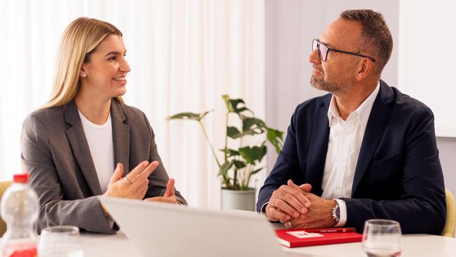 Kandidatin mit Kaufland-Mitarbeiter in einem Konferenzraum der Zentrale beim Bewerbungsgespräch. Auf dem Tisch steht ein aufgeklappter Laptop.