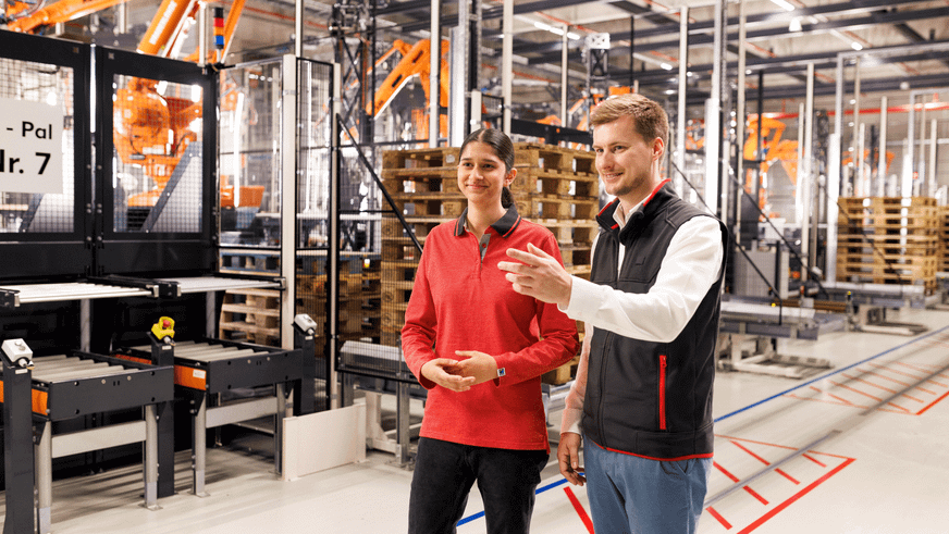 Eine junge Mitarbeiterin und ein Ausbilder arbeiten in der Logistik. Der Ausbilder erklärt etwas.