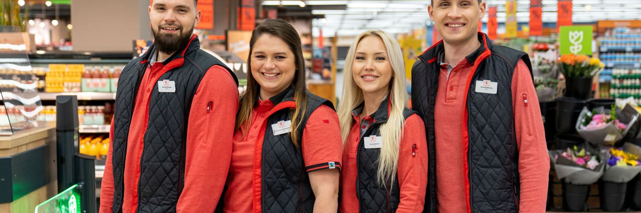 Vier Azubis stehen in einer Kaufland-Filiale und lächeln in die Kamera.