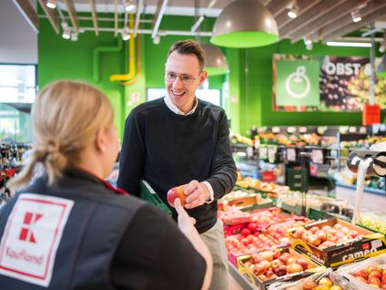 Hausleiter einer Kaufland-Filiale reicht einer Mitarbeiterin einen Apfel.