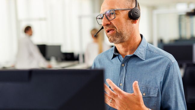 Kaufland-Mitarbeiter mit Headset vor einem Bildschirm in angeregtem Gespräch bei einer Telko.