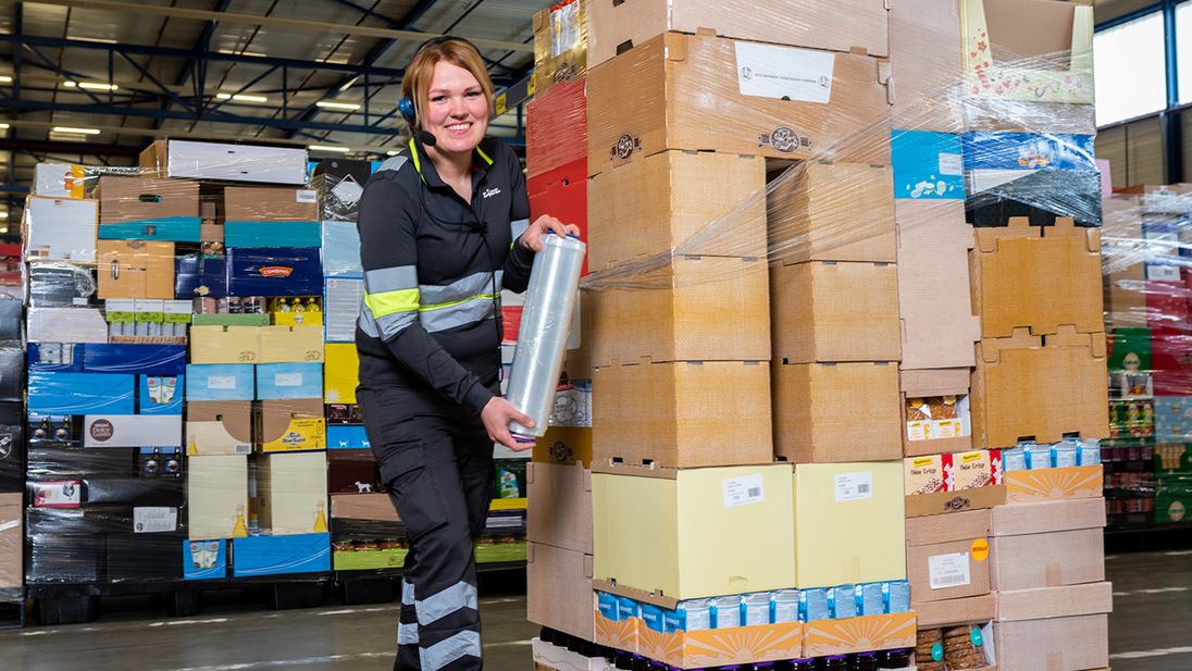 Een Lidl orderpicker wikkelt folie om een pallet met dozen in een magazijn.