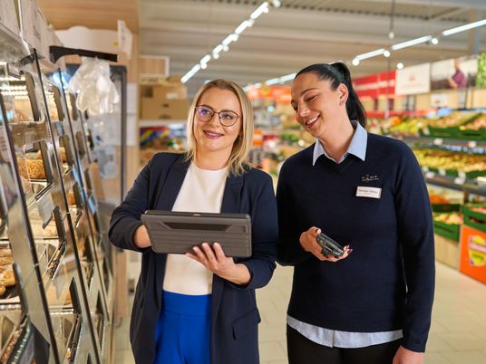Praca w sklepie. Kobieta pracownik sklepu stoi przy lodówce z nabiałem i sprawdza jakość produktów.