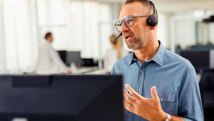 Kaufland-Mitarbeiter mit Headset vor einem Bildschirm in angeregtem Gespräch bei einer Telko.