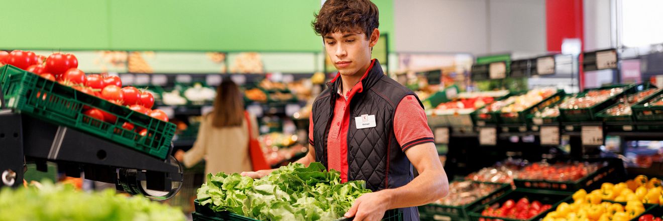Obst- und Gemüsebereich einer Kaufland-Filiale: Junger Verkaufsmitarbeiter verräumt eine Box mit Salat.