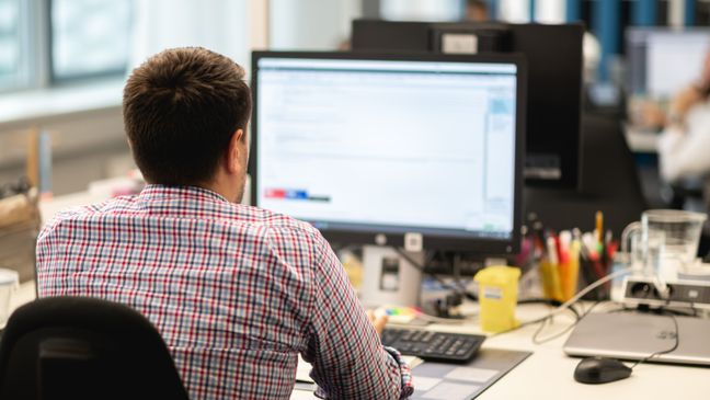 zamestnanec IT oddelenia s desktopovým počítačom sedí v office pri stole