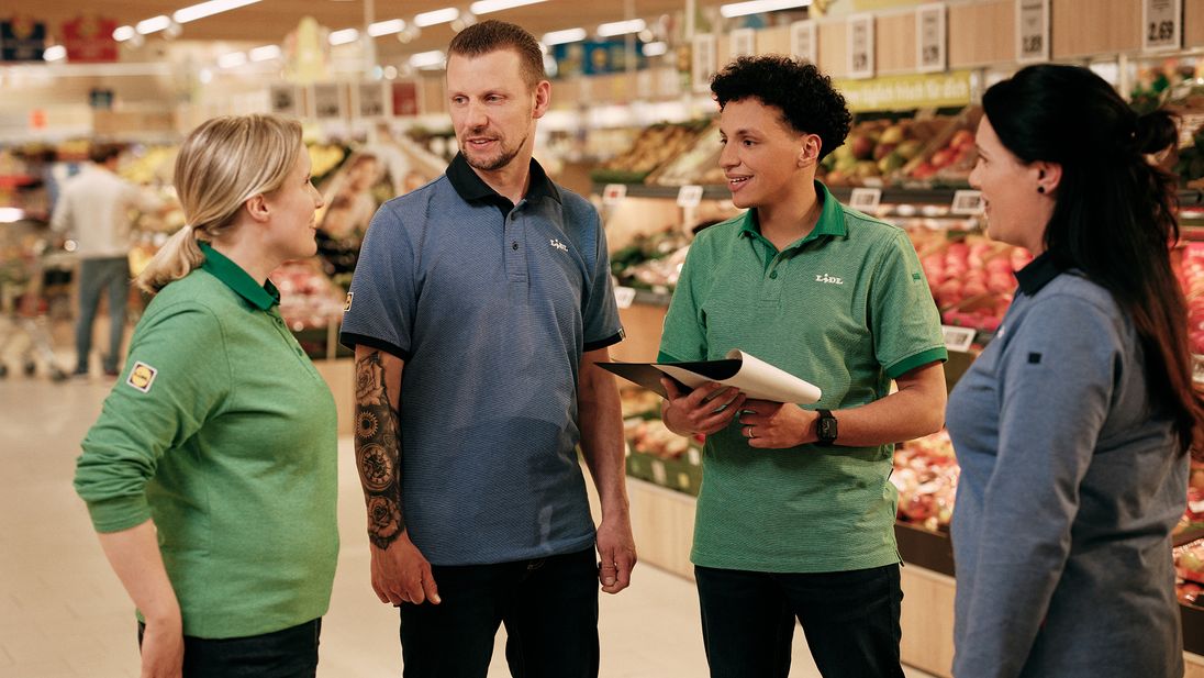 Vier Mitarbeiter in der Obst- und Gemüseabteilung beim Gespräch