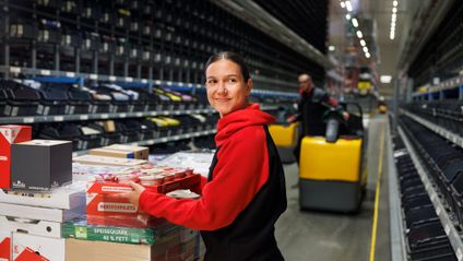 Mitarbeiterin im Kaufland Logistikzentrum beim Kommissionieren von Waren, lächelnd und bereit für den Versand. Karriere bei Kaufland Logistik.