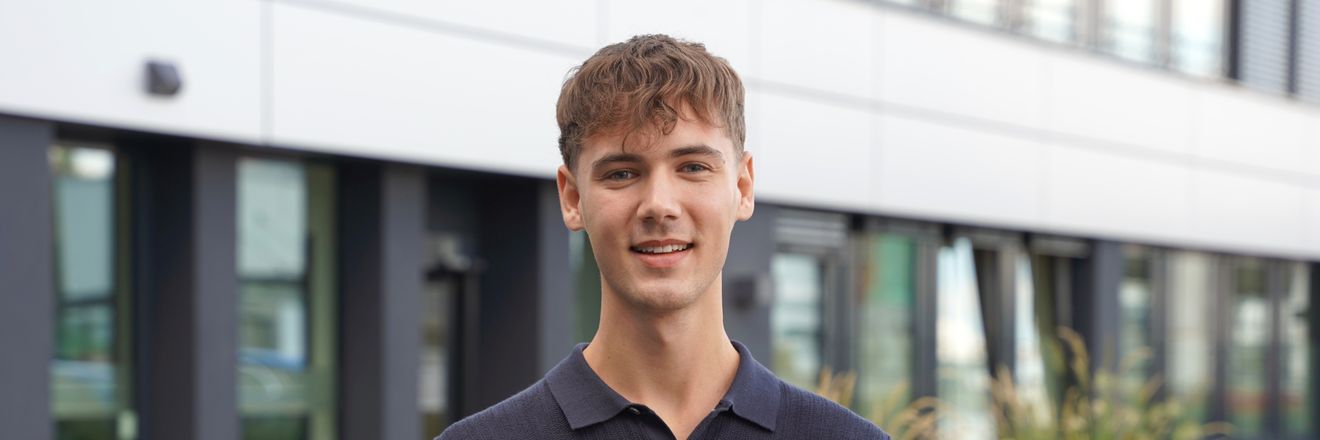 Dualer Student steht vor einem Bürogebäude von Kaufland und lächelt freundlich in die Kamera