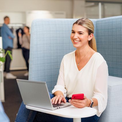 Kaufand-Mitarbeiterin in stylischer Büro-Lounge mit Laptop. Sie ist im Gespräch mit einem Kollegen.