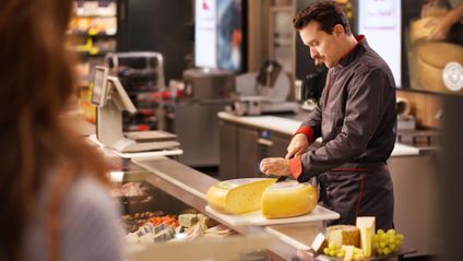 Kaufland-Bedientheke: Ein Verkaufsmitarbeiter schneidet einen Laib Käse auf.