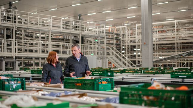 Mitarbeiter bei Kaufland erklärt einer Kollegin etwas in einem Logistikzentrum.
