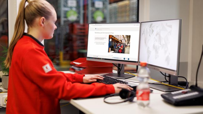 Logistikmitarbeiterin von Kaufland bei der Arbeit am Schreibtisch mit 2 Bildschirmen.