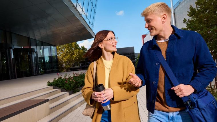 Zwei Mitarbeitende gehen neben einem Bürogebäude und unterhalten sich
