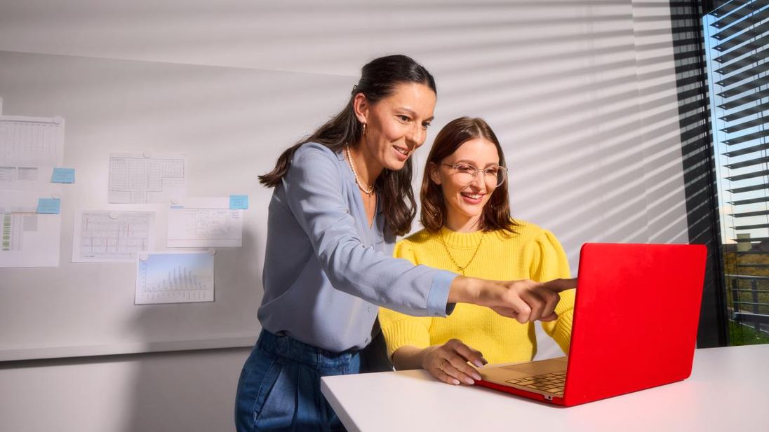 Zwei Mitarbeiterinnen stehen vor einen roten Laptop