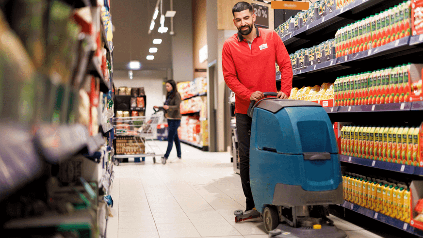 Ein Mitarbeiter in rotem Kaufland-Pullover läuft mit einer Reinigungsmaschine durch die Gänge einer Kaufland-Filiale.