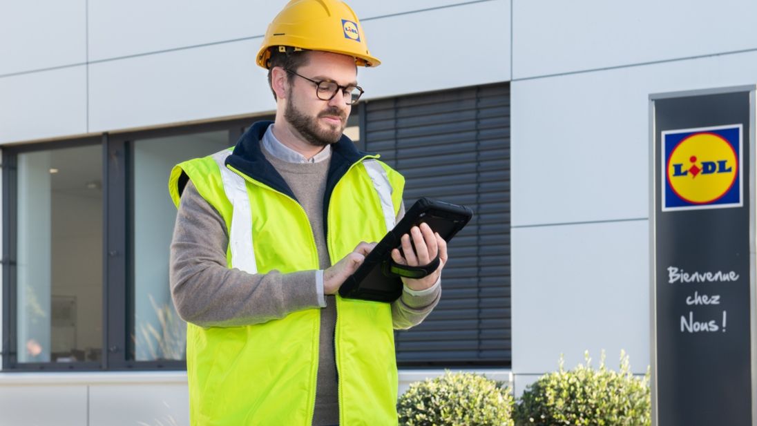Homme avec un gilet de sécurité et casque de chantier, en train de vérifier des informations sur une tablette