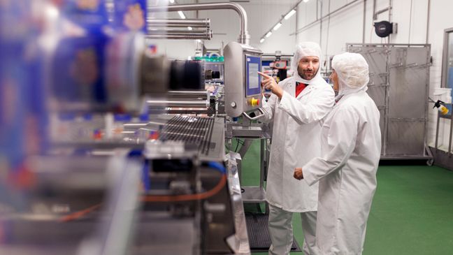 Eine Mitarbeiterin und ein Mitarbeiter in Schutzkleidung in der Betriebsstätte eines Kaufland-Fleischwerks.