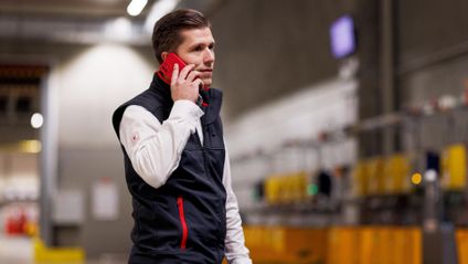 Logistik-Mitarbeiter von Kaufland telefoniert mit seinem Handy beim Gang durchs Lager.