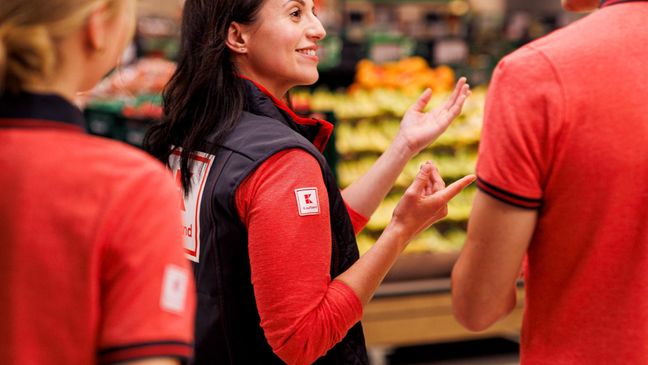 Verkaufsmitarbeiterin von Kaufland im Gespräch mit einem Kollegen. Eine Kollegin, die im Bildvordergrund abgebildet ist, hört zu.