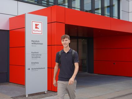 Dualer Student läuft aus dem Bürogebäude von Kaufland International und lächelt freundlich.