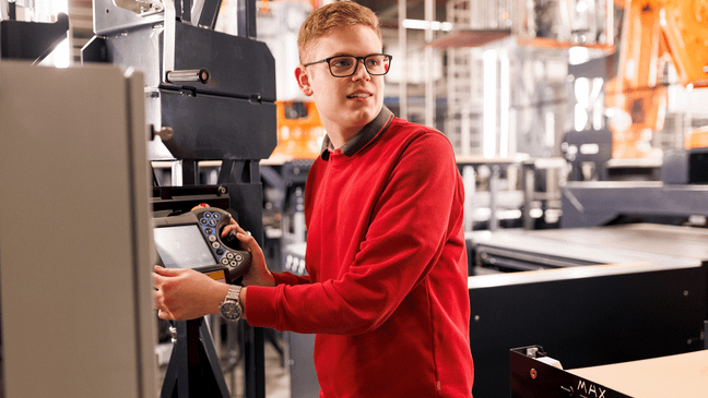 Ein Mitarbeiter in rotem Pullover bedient eine Maschine bzw. eine Anlage.