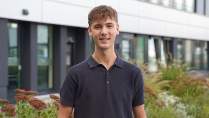 Dualer Student steht vor einem Bürogebäude von Kaufland und lächelt freundlich in die Kamera