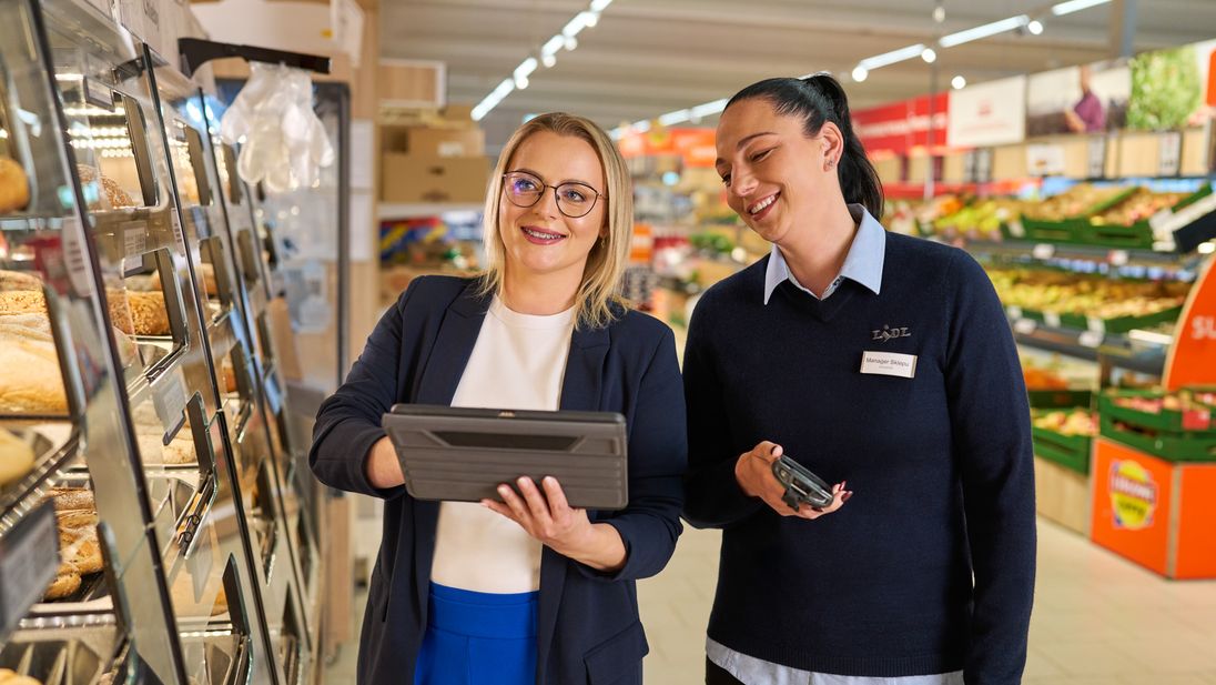Praca w sklepie. Kobieta pracownik sklepu stoi przy lodówce z nabiałem i sprawdza jakość produktów.