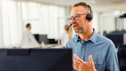 Kaufland-Mitarbeiter mit Headset vor einem Bildschirm in angeregtem Gespräch bei einer Telko.