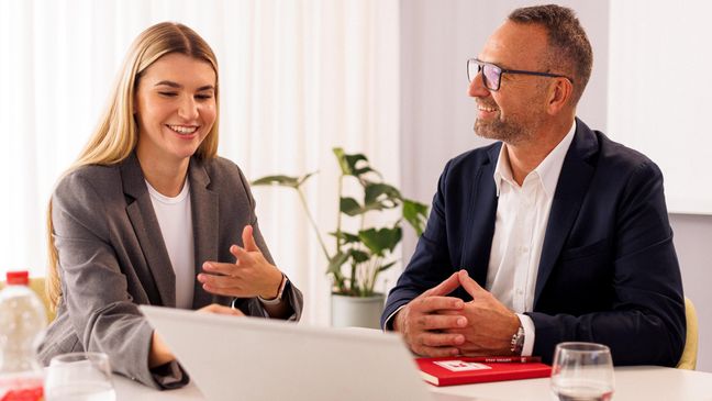 Kandidatin mit Kaufland-Mitarbeiter in einem Konferenzraum der Zentrale beim Bewerbungsgespräch. Auf dem Tisch steht ein aufgeklappter Laptop.
