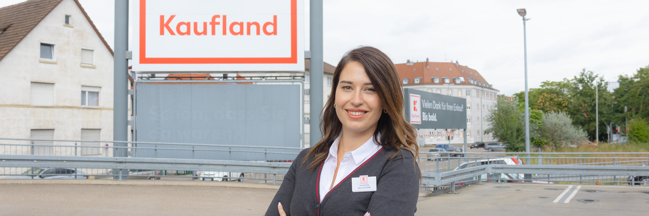 Hausleiterin und ehemalige Trainee steht vor Kaufland-Filiale und lächelt in die Kamera.