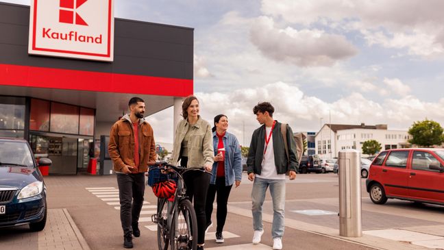 Mitarbeiter und Azubis, zwei junge Frauen, zwei junge Männer, alle in Freizeitkleidung entfernen sich nach Feierabend von einer Kaufland-Filiale.
